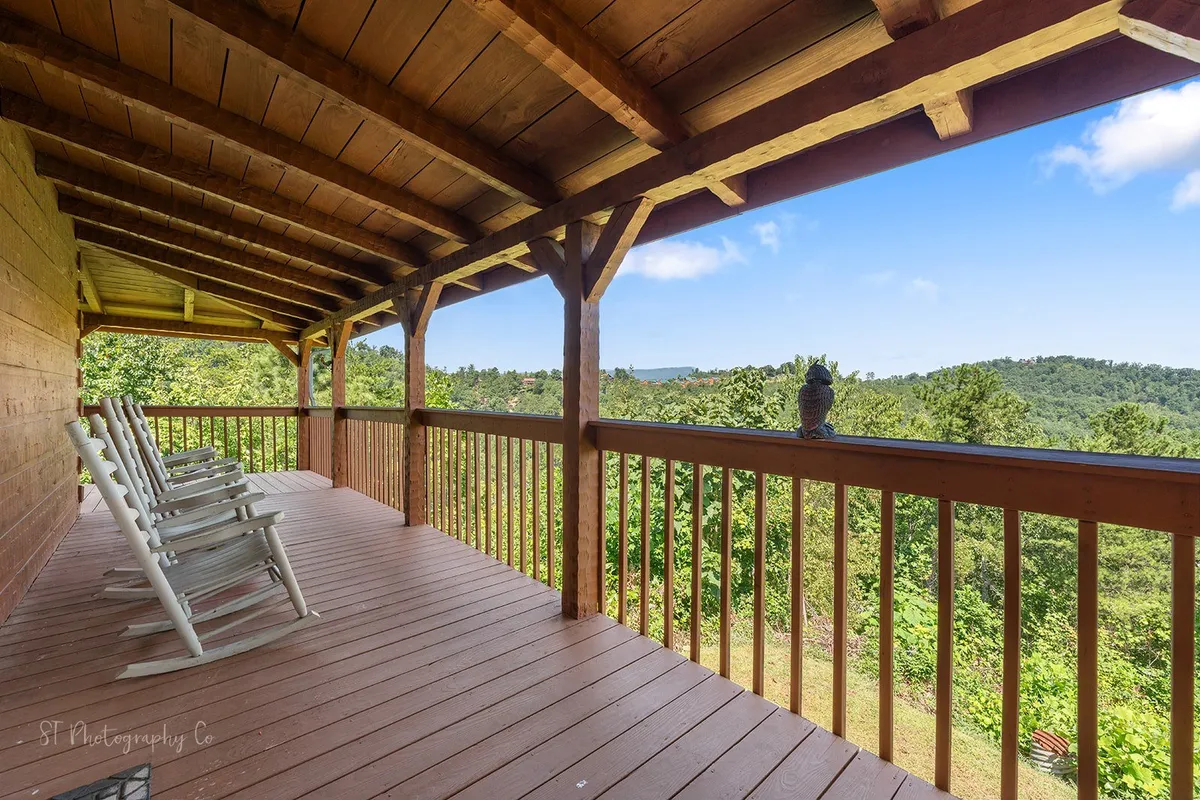 An inviting exterior deck scene with sturdy rocking chairs facing out over a wooden railing, framing a sweeping scenic view of the mountains. The setting is perfect for both quiet moments and socializing, with ample space and a peaceful ambiance.
