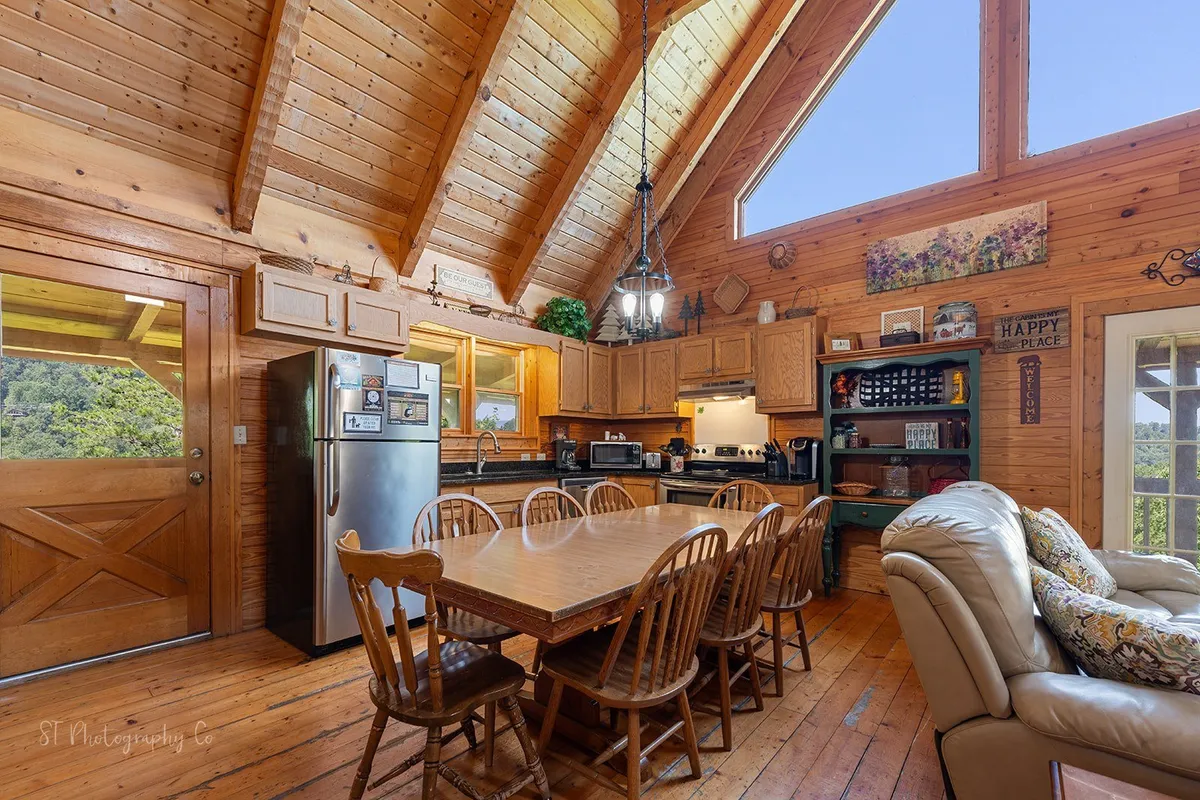 A bright and open dining area with a large table, modern kitchen, expansive windows, and exposed wooden beams. The space is filled with natural light, perfect for family meals, celebrations, or casual gatherings after a day exploring local attractions.