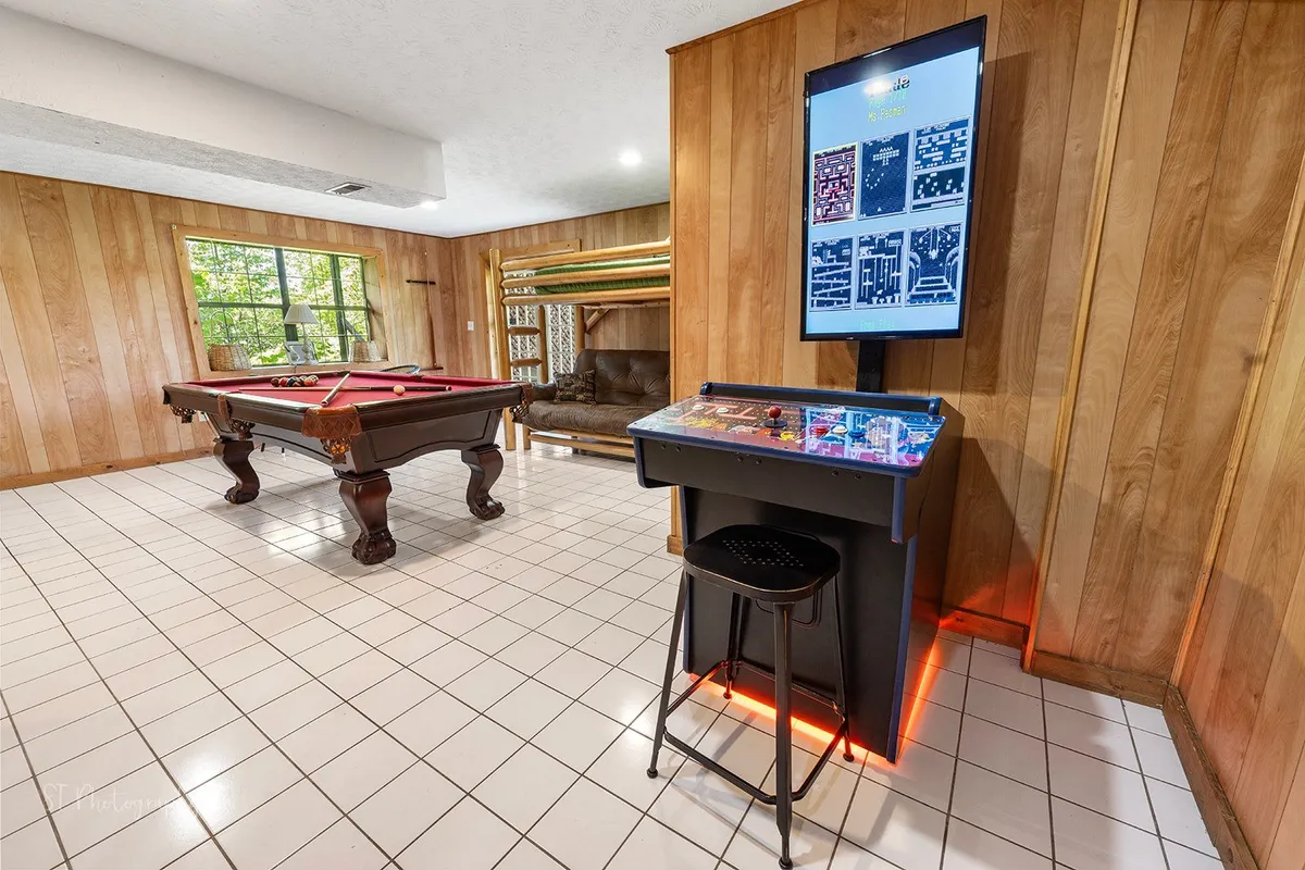 A vibrant game room scene with a pool table, an arcade game, and a comfortable sitting area arranged for socializing. The atmosphere is fun and relaxed, with space for multiple types of entertainment and gatherings.