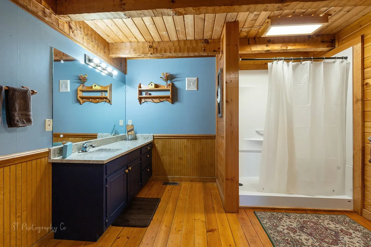 A stylish bathroom with a vanity, sink, and shower area accented by warm wooden beams and decorative shelves. The inviting, well-lit space offers privacy and comfort, ensuring guests can enjoy personal grooming and relaxation routines.