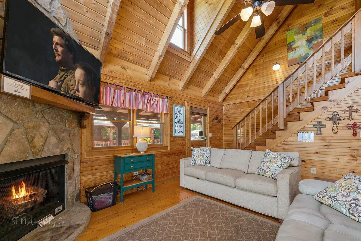 A cozy living area with a glowing fireplace, a spacious sofa, a flat-screen TV, and large windows letting in natural light. The decor is inviting, perfect for gathering around the fire, streaming a movie, or sharing stories on a cool evening.