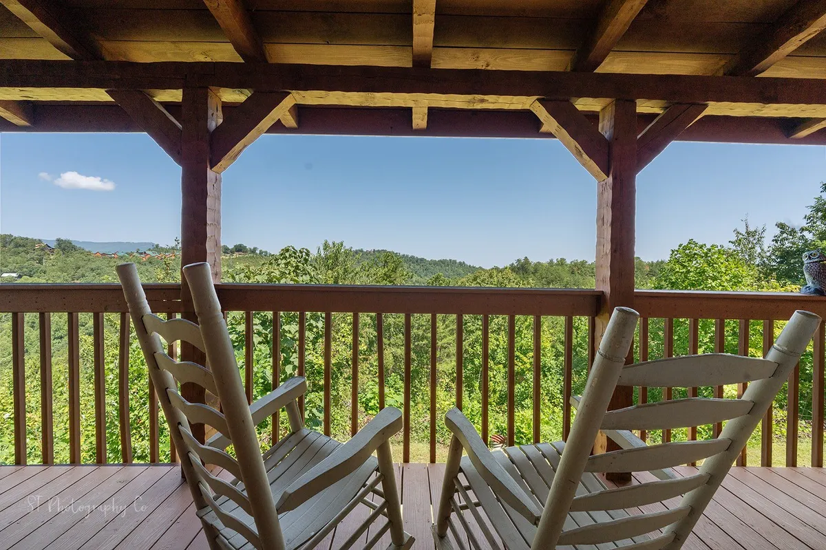 A covered deck with rustic wooden railings and a pair of classic rocking chairs, offering panoramic mountain views. The space is sheltered overhead, making it ideal for enjoying a coffee at sunrise or relaxing with a book while immersed in the fresh mountain air.